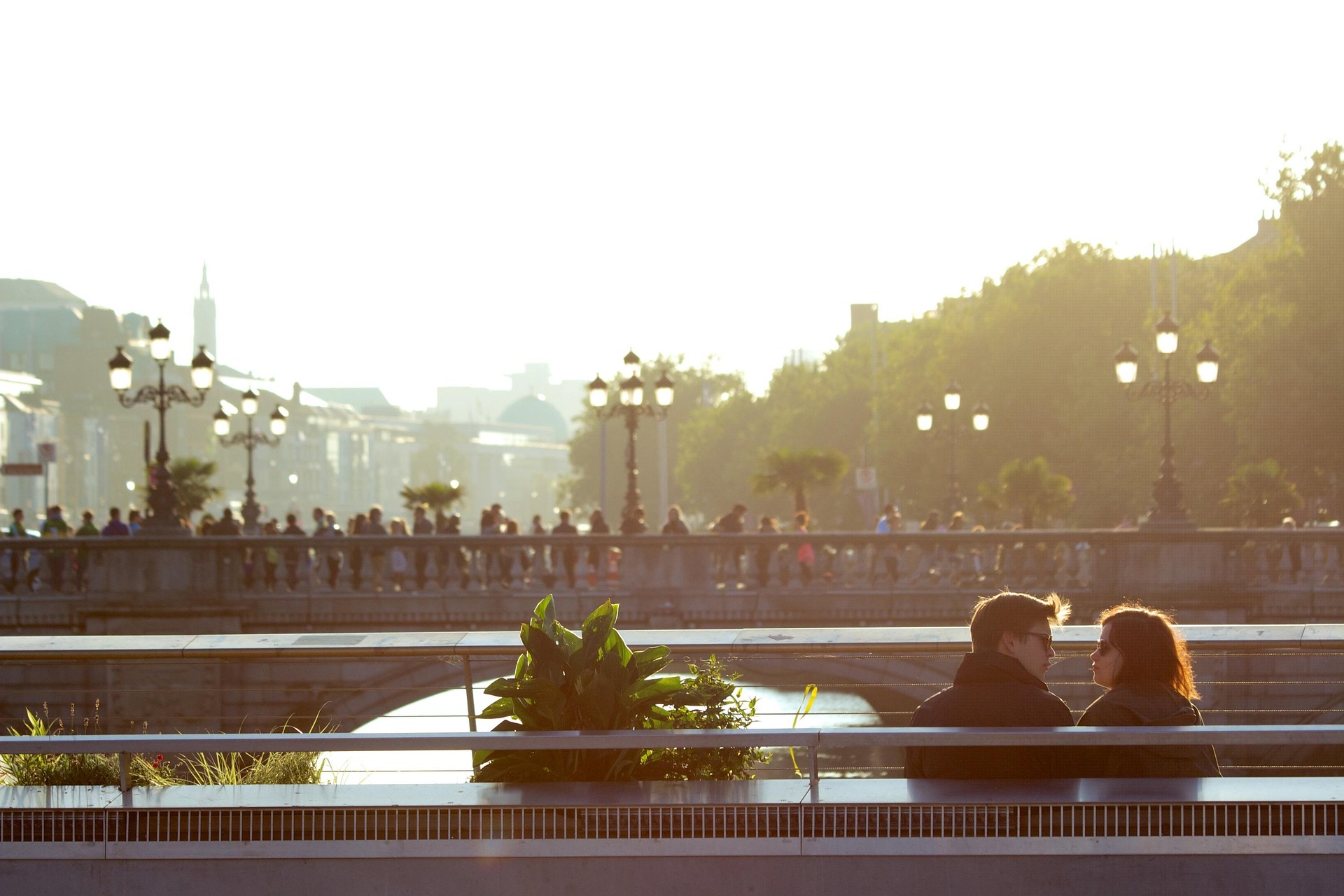 A couple sitting on a bench at golden hour, looking out over a city and bridge.